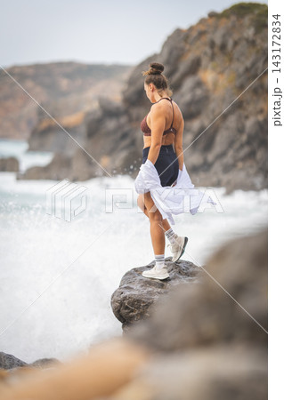 Woman standing on a rock by ocean waves on a cloudy day at a coastal location 143172834