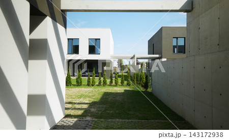 Contemporary housing complex with geometric facades, concrete structures, green lawns, and planted trees under a clear blue sky 143172938