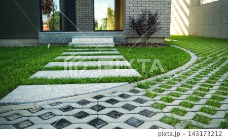 Contemporary residential exterior featuring a minimalist walkway, lush lawn, and eco-friendly driveway pavement design 143173212