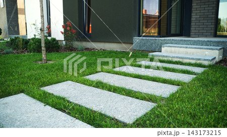 Granite stepping stones form a path across vibrant green grass, leading to a modern home that blends architecture with nature Granite stepping stones form a path across vibrant green grass, leading to a modern home that blends architecture with nature 143173215