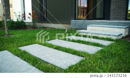 Modern stepping stones leading to contemporary house entrance with green lawn and garden landscaping Modern stepping stones leading to contemporary house entrance with green lawn and garden landscaping 143173216