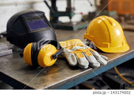 Essential industrial safety equipment including a welding helmet and hard hat on a metal workbench 143174802