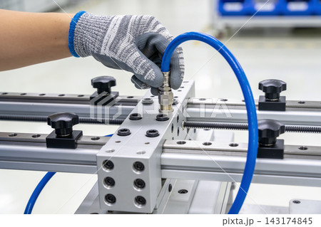 Technician connecting a blue pneumatic hose to a precision aluminum industrial machine component 143174845