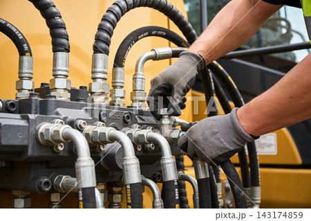 Mechanic performing maintenance on heavy construction machinery hydraulic system components 143174859
