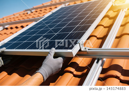 Professional technician installing solar panels on a residential clay tile roof at sunny day Professional technician installing solar panels on a residential clay tile roof at sunny day 143174883