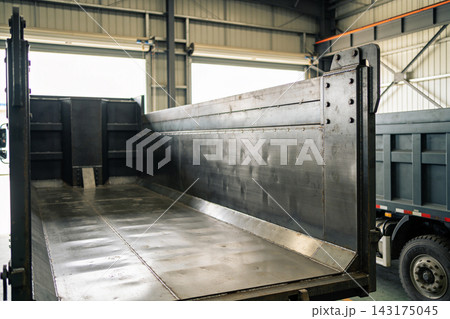 Heavy duty steel dump truck trailer bed parked inside a large industrial manufacturing workshop 143175045