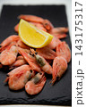 Frozen shrimps are laid out on a gray background on a black slate, with a bright half of a lemon placed on top. Concept: cool color contrast, the aesthetics of minimalistic snack serving. High quality 143175317