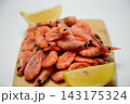 Close-up of a wooden board with a handful of frozen pink shrimp and two lemon slices around the edges on a blurred light background. Concept: detailing of the ice cream product, minimalistic citrus 143175324