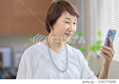オフィスでスマホを見る60代女性 オフィスでスマホを見る60代女性 143175800