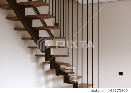 Modern floating staircase with wooden steps and black metal railings. A stack of books rests on the steps of contemporary staircase, minimalist design Modern floating staircase with wooden steps and black metal railings. A stack of books rests on the steps of contemporary staircase, minimalist design 143175809