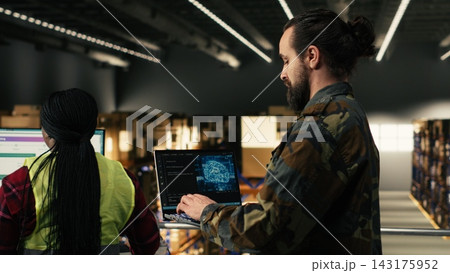 Military officer using AI-powered tools in warehouse at military base, monitoring artificial intelligence software on laptop. Machine learning and neural networks supporting tactical operations. Military officer using AI-powered tools in warehouse at military base, monitoring artificial intelligence software on laptop. Machine learning and neural networks supporting tactical operations. 143175952