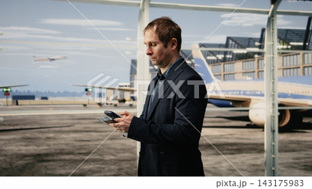 Businessman using phone inside modern airport terminal to do online check in. Digital nomad using smartphone to access internet airline website and check plane timetable 143175983