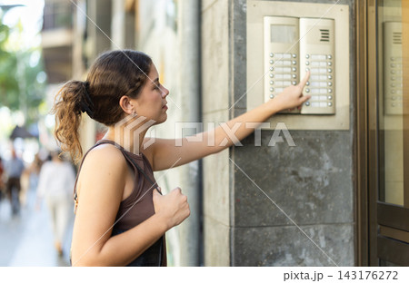 Young woman pressing button to ring outdoor intercom 143176272