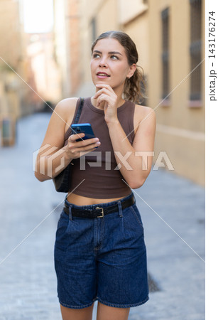 Girl walks around city district with mobile phone 143176274