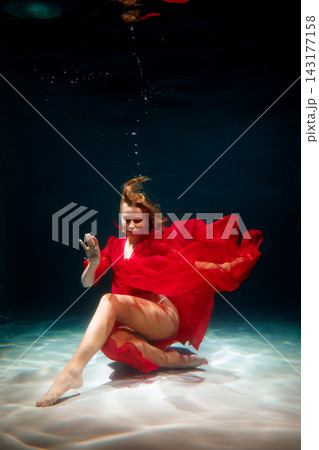 Underwater scene featuring woman in vibrant red dress flowing freely Underwater scene featuring woman in vibrant red dress flowing freely 143177158