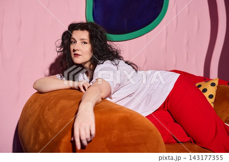 Stylish woman resting confidently on orange sofa with artistic backdrop 143177355