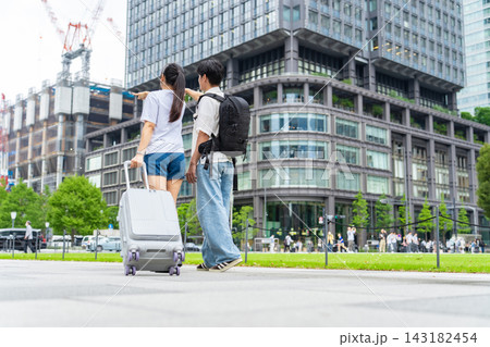 街を歩く観光客カップルの後ろ姿。旅行、観光、インバウンド、外国人、歩行者、荷物、日本、都会、ツアー 143182454