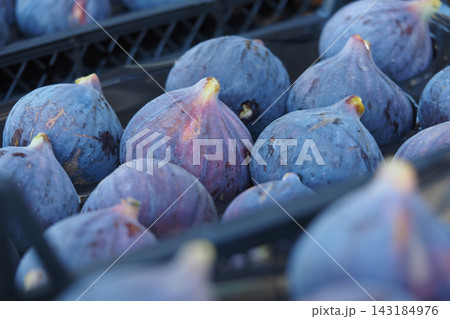 Figs are artfully arranged within a black basket situated in a lively market setting 143184976