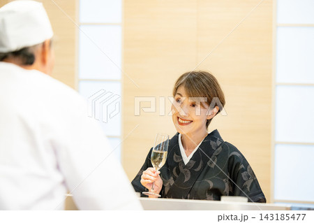 寿司屋のカウンターで大将と会話するシニア女性客 寿司屋のカウンターで大将と会話するシニア女性客 143185477