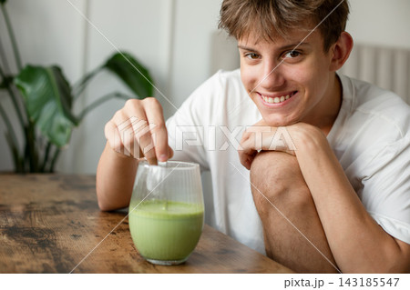 Happy teenager looking at camera and mixing fresh green matcha latte drink at home 143185547