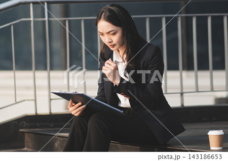 Young brunette business lady dressed in black jacket checking work chats sitting outside with laptop Young brunette business lady dressed in black jacket checking work chats sitting outside with laptop 143186653