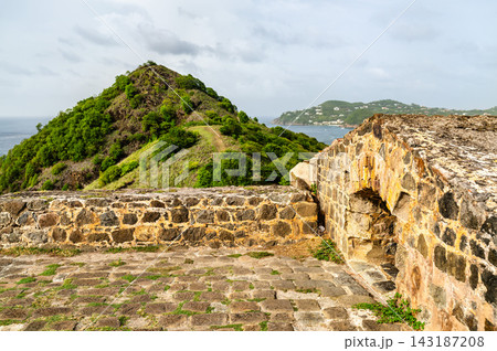 Historic stone fortification walls at Fort Rodney on Pigeon Island overlooking the green hills and Caribbean Sea in Saint Lucia. Historic stone fortification walls at Fort Rodney on Pigeon Island overlooking the green hills and Caribbean Sea in Saint Lucia. 143187208