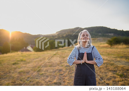 Senior woman practicing meditation outdoors in peaceful countryside. 143188064