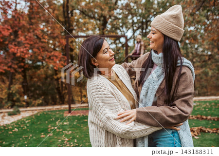 Mature daughter with older mom standing in the middle of autumn park. 143188311