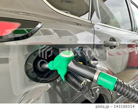 Green petrol nozzle inserted into the fuel tank of a dark car at station. Concept of automatic refueling process, alternative energy resources, and modern vehicle ownership Green petrol nozzle inserted into the fuel tank of a dark car at station. Concept of automatic refueling process, alternative energy resources, and modern vehicle ownership 143188314