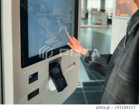 Teenage girl using touch screen interactive display to order food at self service kiosk. Concept of automated ordering system, youth using technology, and fast food digital experience. 143188317
