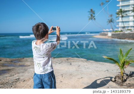 Child capturing memories on smartphone at tropical island getaway Child capturing memories on smartphone at tropical island getaway 143189379