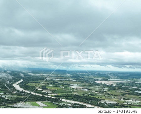Rain clouds blanket swollen river winding through lush agricultural fields, dense mist rolls across the flooded rural landscape in gloomy monsoon day. Rain clouds blanket swollen river winding through lush agricultural fields, dense mist rolls across the flooded rural landscape in gloomy monsoon day. 143191648
