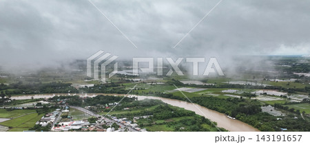 Heavy mist and continuous drizzle cover a winding river and lush agricultural fields in a gloomy rural landscape. Heavy mist and continuous drizzle cover a winding river and lush agricultural fields in a gloomy rural landscape. 143191657
