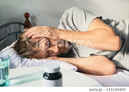 Man having severe headache in bed with medication and water on nightstand Man having severe headache in bed with medication and water on nightstand 143194805