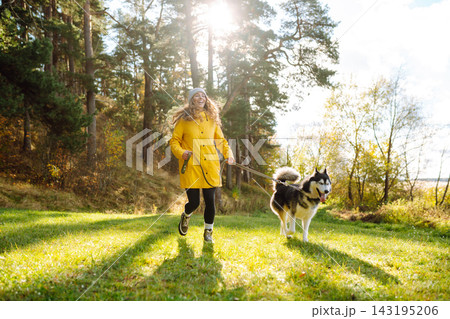 Young woman walks with her husky on lawn in the park. Happy female posing outdoors with her dog. Young woman walks with her husky on lawn in the park. Happy female posing outdoors with her dog. 143195206