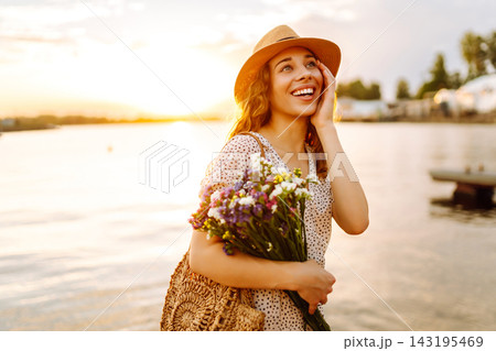 Happy woman sitting on wooden and clutched bouquet of wildflowers tightly in hand. Travel concept. 143195469