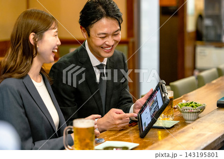 居酒屋でタブレット注文をするスーツの男女 143195801