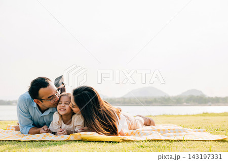 Asian family father mother and daughter lying on blanket spring meadow field grass in park cheerful sweet kid girl, parents and child picnic enjoying outdoors sunset time together Asian family father mother and daughter lying on blanket spring meadow field grass in park cheerful sweet kid girl, parents and child picnic enjoying outdoors sunset time together 143197331