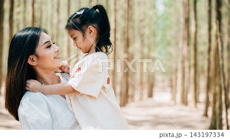 Asian mother carrying a daughter in arms in a peaceful forest setting, Happy smile mother and little child playing together outdoor 143197334