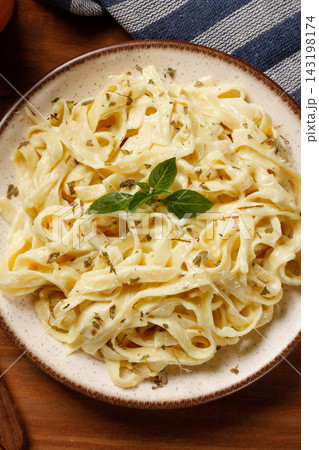 Fettuccine Alfredo with cheese sauce on a rustic plate, accompanied by fresh basil, on a rustic table. 143198174