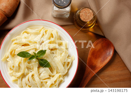 Creamy Fettuccine Alfredo with cheese sauce, served in a white bowl with fresh basil on a wooden table. Creamy Fettuccine Alfredo with cheese sauce, served in a white bowl with fresh basil on a wooden table. 143198175