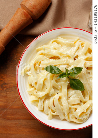 Creamy Fettuccine Alfredo with white cheese sauce served in a white bowl, finished with fresh basil, on a wooden table. Creamy Fettuccine Alfredo with white cheese sauce served in a white bowl, finished with fresh basil, on a wooden table. 143198176