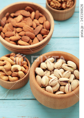 Mixed nuts in wooden bowls on blue wooden background. Almonds, pistachio, walnuts, cashew, hazelnut. Vertical photo Mixed nuts in wooden bowls on blue wooden background. Almonds, pistachio, walnuts, cashew, hazelnut. Vertical photo 143198626