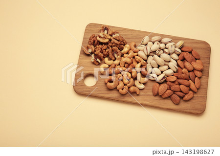 Mix of various nuts on cutting board on beige background. Pistachios, cashews, walnuts, hazelnuts, peanuts. 143198627
