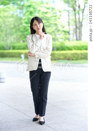 口をすぼめてあごに手を当て悩むスーツ姿の女性 口をすぼめてあごに手を当て悩むスーツ姿の女性 143198722