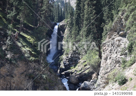 Mountain Waterfall in Kyrgyzstan Surrounded by Coniferous Forest and Rocky Mountains Mountain Waterfall in Kyrgyzstan Surrounded by Coniferous Forest and Rocky Mountains 143199098