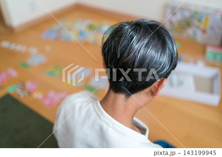 床に座ってボードゲームを一人で楽しむ13歳の男の子の後ろ姿 143199945