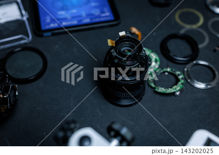 Disassembled camera lens and optical parts on a dark workbench beside a tablet, detailed electronics repair and photography equipment maintenance. Disassembled camera lens and optical parts on a dark workbench beside a tablet, detailed electronics repair and photography equipment maintenance. 143202025