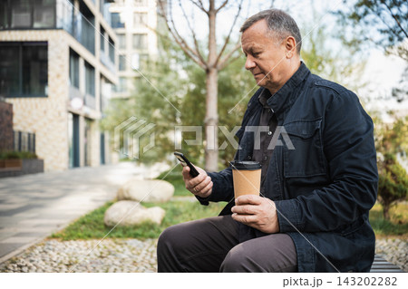 Man using smartphone with takeaway coffee outdoors 143202282