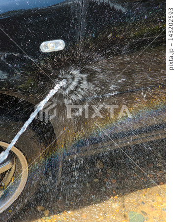 Water Spray Creates Rainbow on Dark Car During Washing 143202593